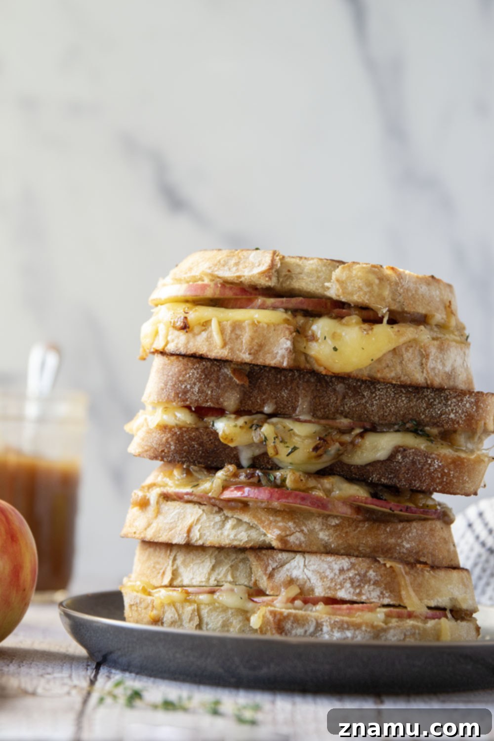 A vibrant display of fresh ingredients for apple butter caramelized onion grilled cheese: apples, cheese, ciabatta, and onions.