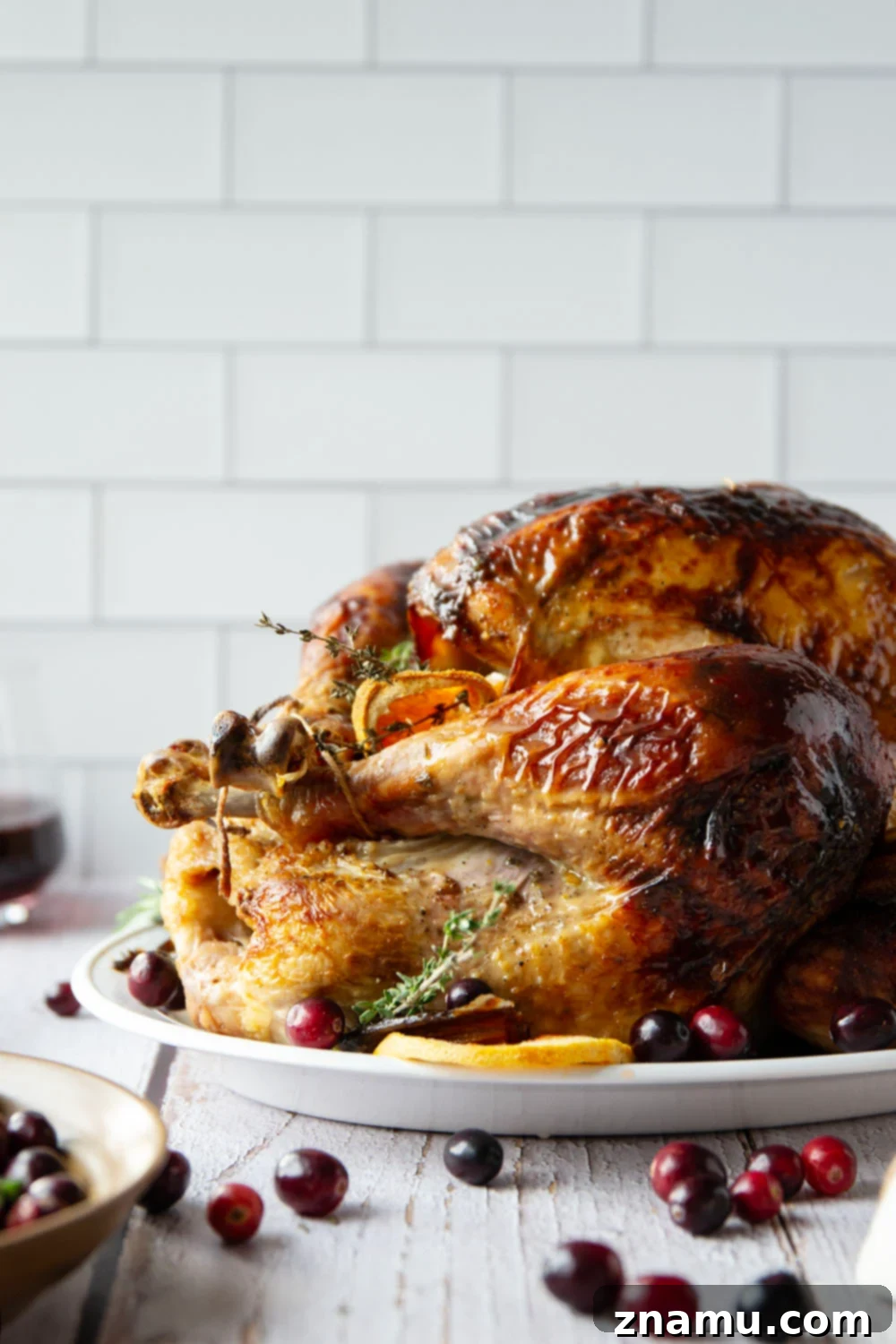 Golden Maple Turkey Roast 5 A whole roasted Maple Glazed Turkey presented on a platter, still intact before carving. The glaze is visible, and the turkey is garnished with fresh herbs and orange slices, emphasizing its readiness for a festive meal.