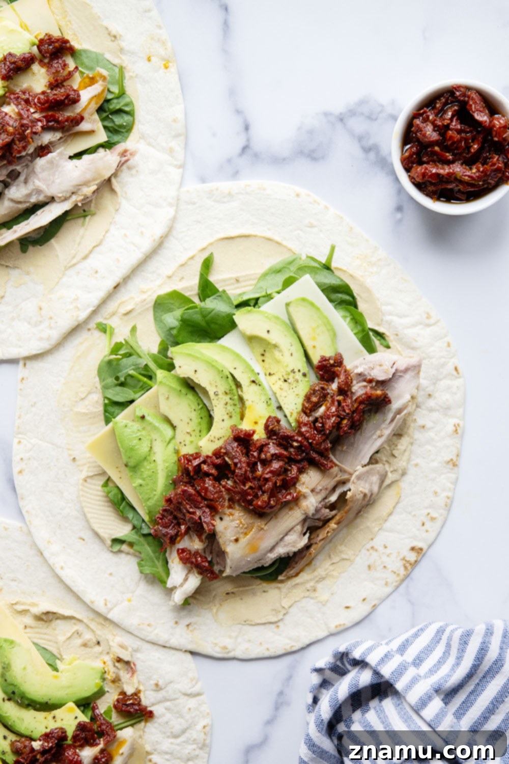 Mediterranean Turkey Hummus Wrap with Sun-Dried Tomatoes 3 Close-up of a freshly made turkey hummus wrap, showing layers of turkey, cheese, avocado, and sun-dried tomatoes.