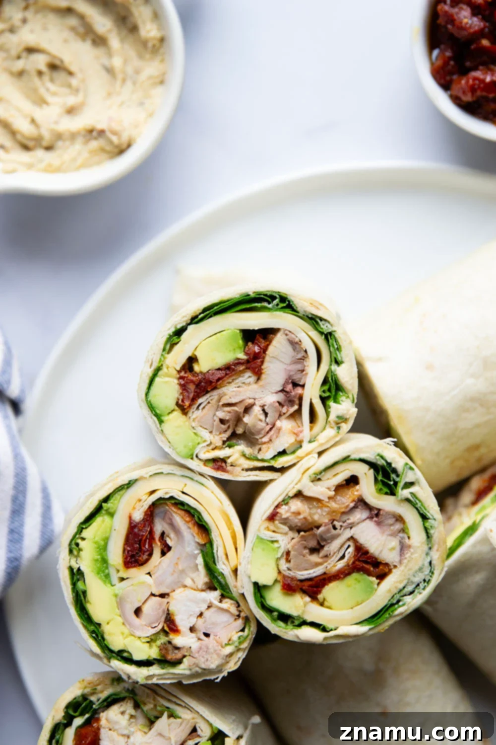 Mediterranean Turkey Hummus Wrap with Sun-Dried Tomatoes 4 Assortment of fresh ingredients for turkey hummus wraps laid out, including turkey, cheese, hummus, avocado, and sun-dried tomatoes.