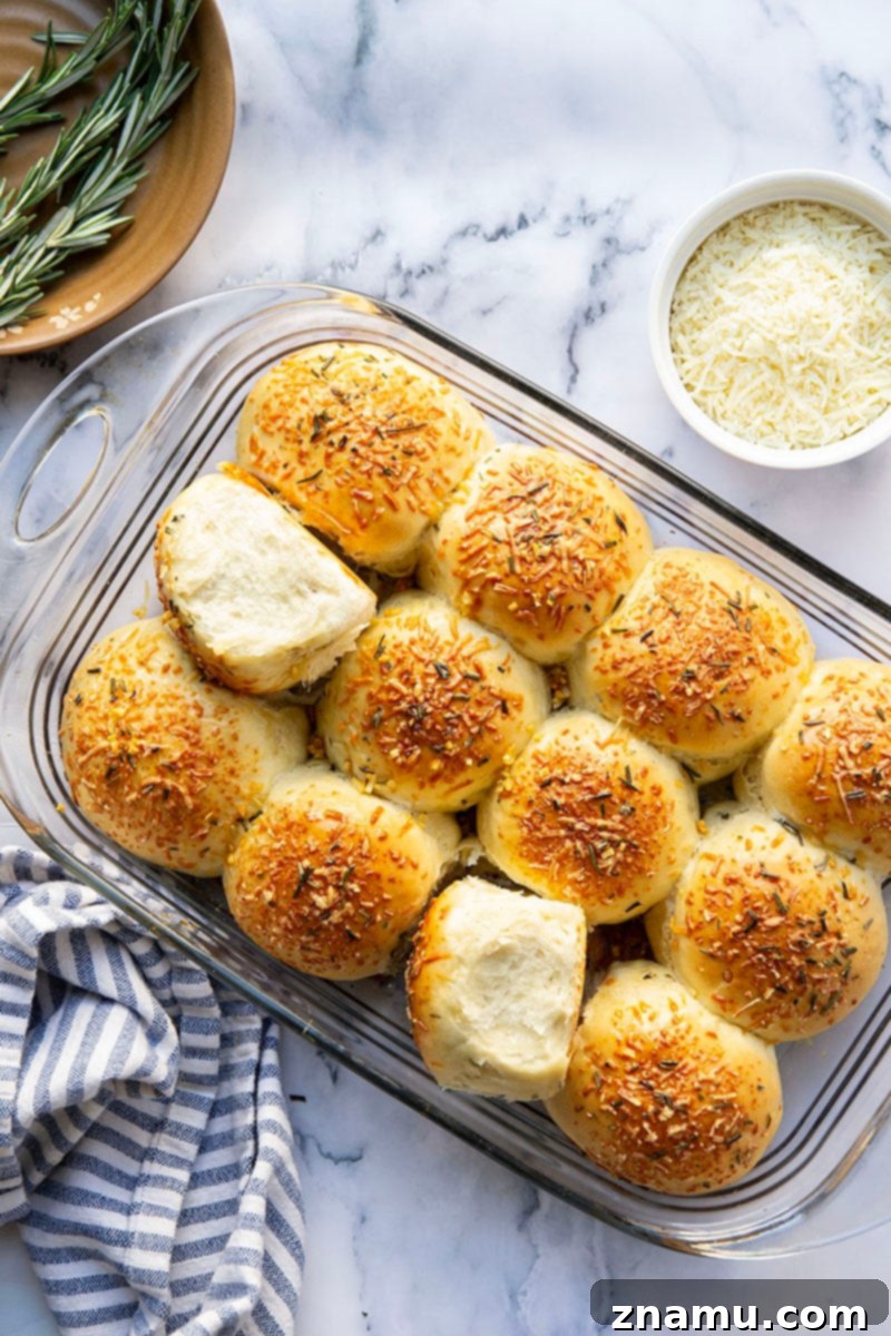Your Thanksgiving Feast Roadmap 20 Freshly baked Asiago Rosemary Dinner Rolls, golden brown and soft, arranged on a cooling rack, garnished with rosemary sprigs.