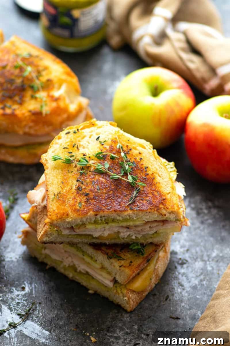 Your Thanksgiving Feast Roadmap 31 A pressed Apple Gouda Pesto Turkey Panini, golden brown with melted cheese oozing, sliced in half and ready to eat.