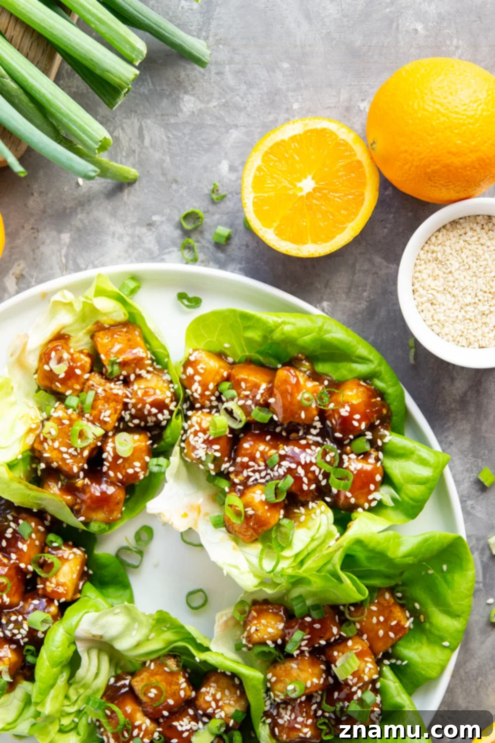 Crispy baked tofu is tossed with a sweet homemade orange sauce and then piled in butter lettuce leaves with lots of green onions and sesame seeds on top.