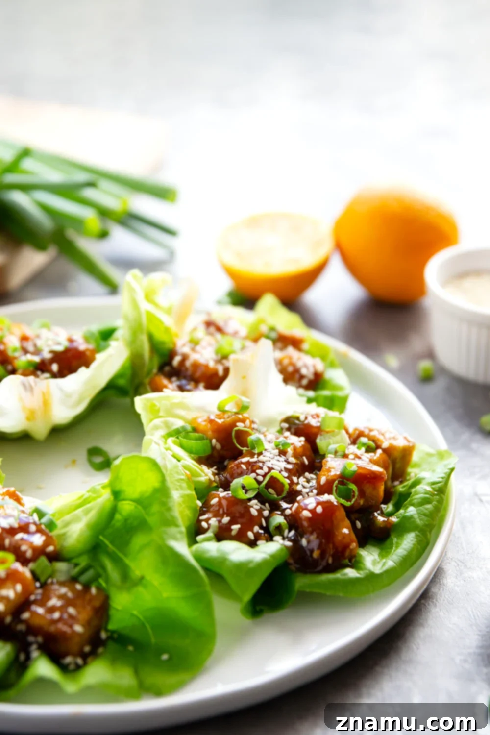 Orange tofu lettuce wraps piled with green onions and sesame seeds on top.