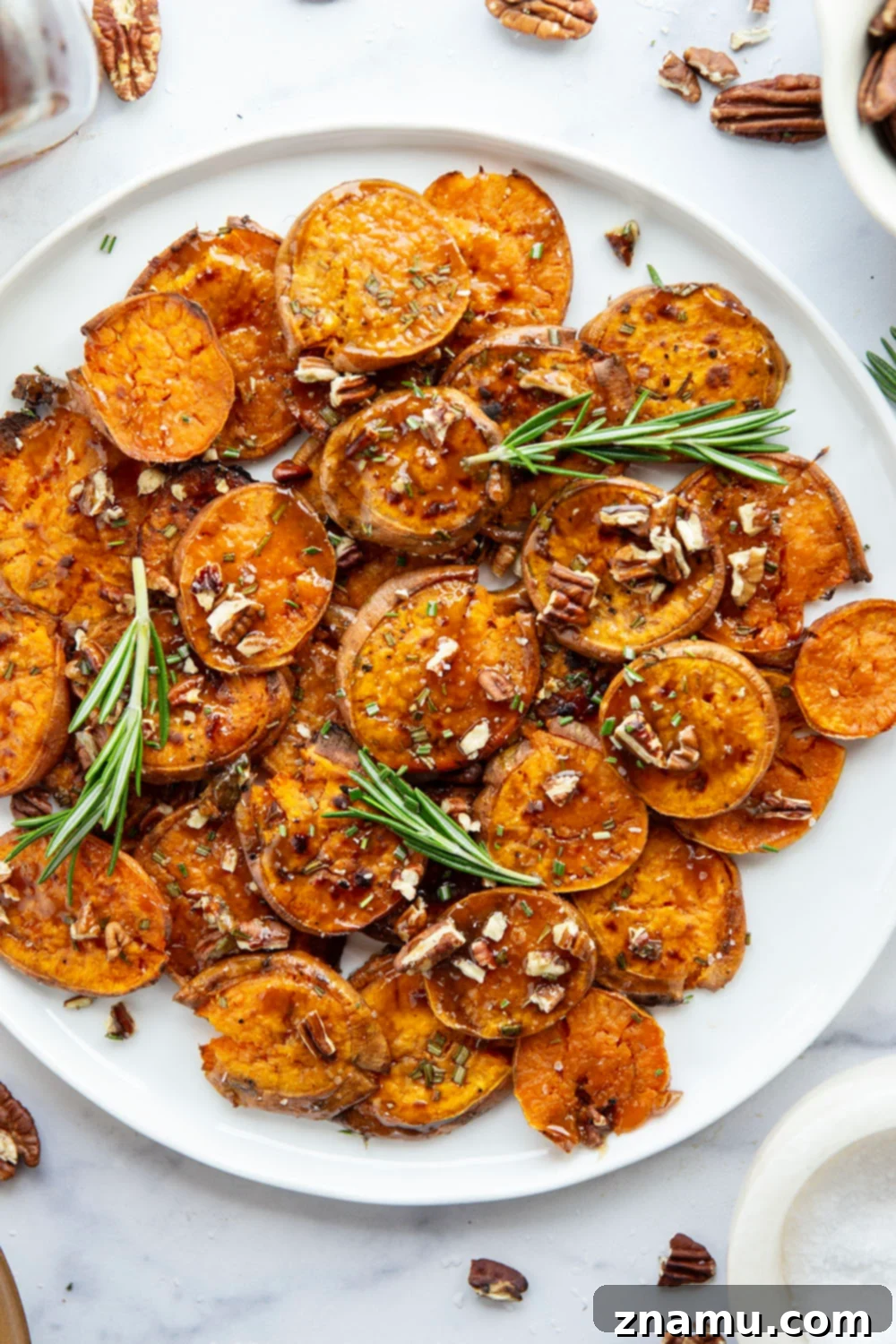 A serving of smashed sweet potatoes with maple glaze, rosemary, and pecans.