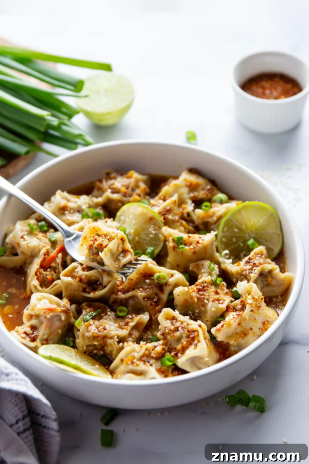Close-up of freshly made spicy chicken wontons drizzled with chili lime sauce and garnishes