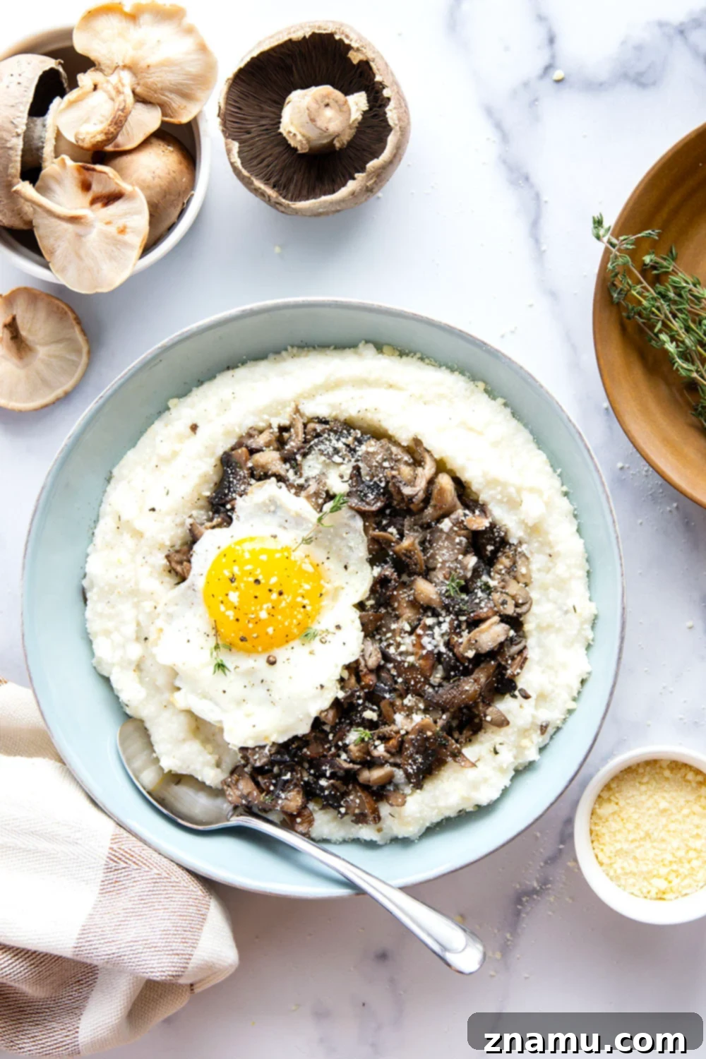 A serving of creamy grits topped with sautéed wild mushrooms and a fried egg, garnished with fresh herbs.