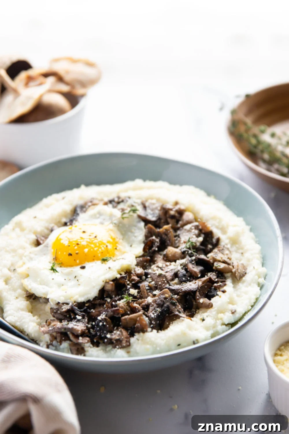 A beautifully plated bowl of wild mushroom grits with a runny fried egg and shredded cheese.