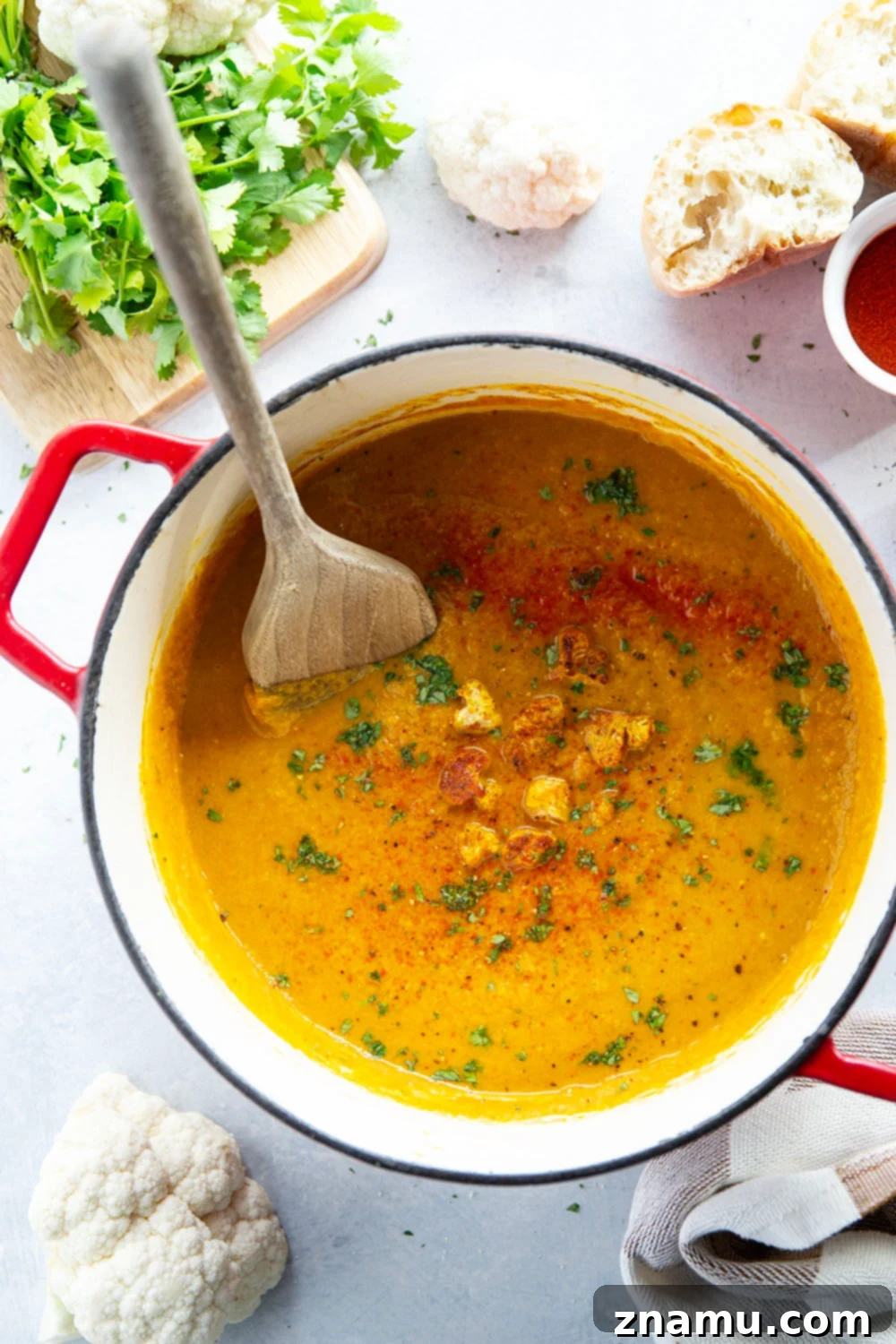 Spiced Moroccan Cauliflower Velvet 6 A cozy table setting featuring a generous bowl of Moroccan Cauliflower Soup, perfectly accompanied by crusty French bread for dipping, and garnished with fresh herbs, inviting a comforting meal.