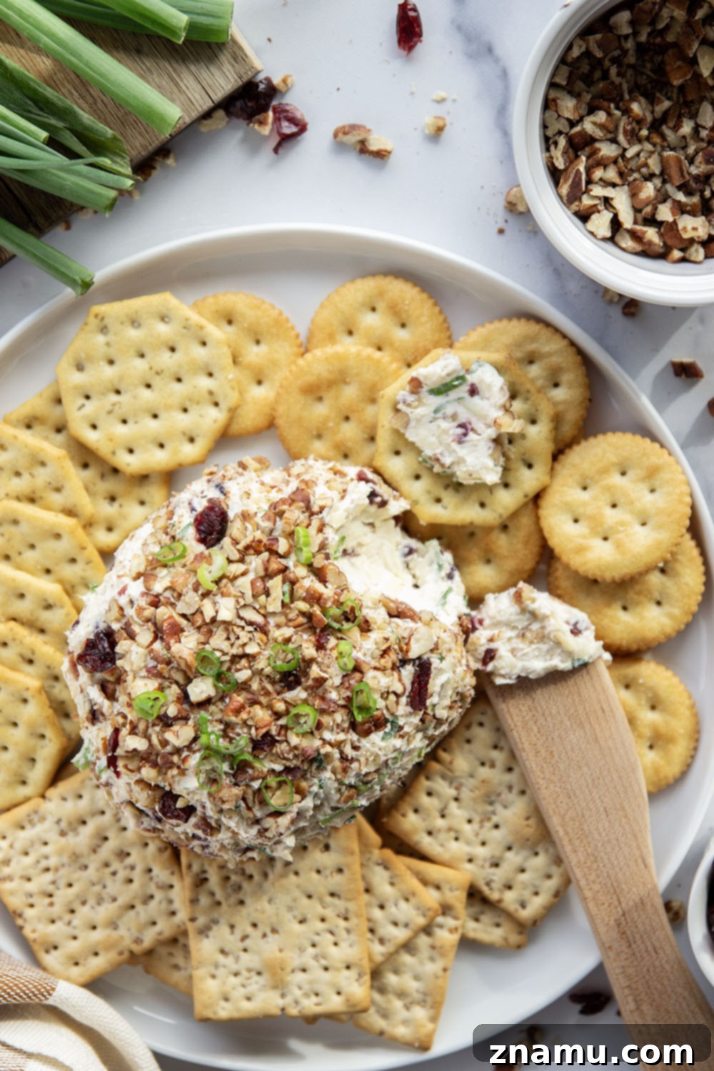 Smoky Cranberry Cheese Delight 6 A hand reaching for a cracker topped with the creamy Smoked Cranberry Cheese Ball, served on a rustic wooden board with a variety of dippers and festive decor.
