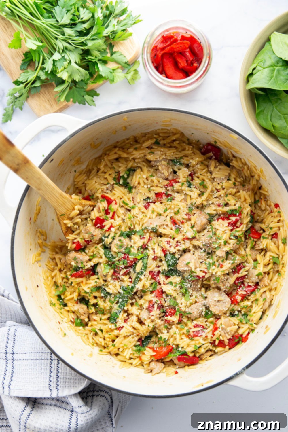 Easy One Pot Chicken Sausage Orzo 2 A vibrant close-up of One Pot Chicken Sausage Orzo, showcasing tender orzo, savory chicken sausage bits, bright red roasted peppers, and wilted green spinach, garnished with fresh parsley and Parmesan cheese.