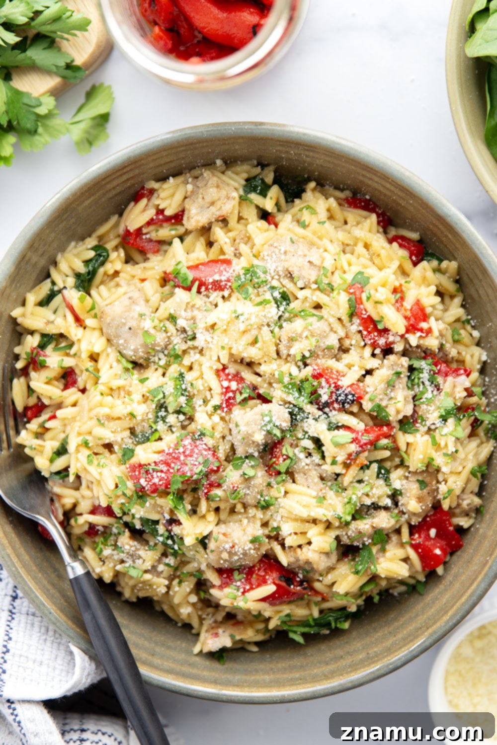 Easy One Pot Chicken Sausage Orzo 5 Raw ingredients laid out for One Pot Chicken Sausage Orzo, including a bowl of orzo, a package of chicken sausage, a jar of roasted red peppers, and fresh spinach.