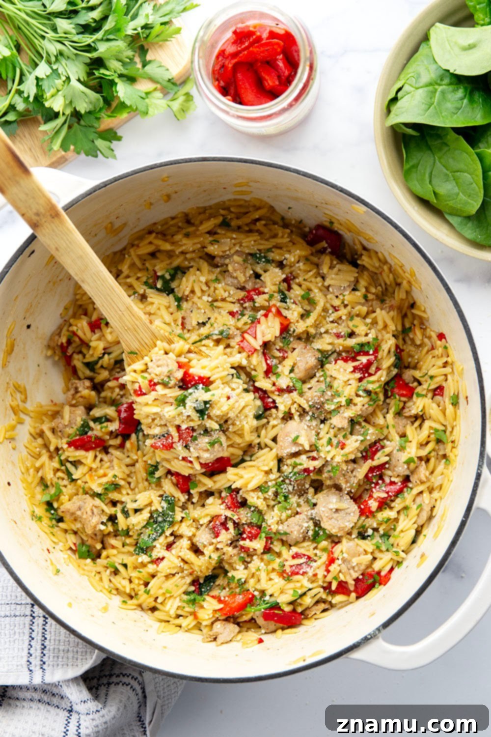 Easy One Pot Chicken Sausage Orzo 6 A close-up of a spoon scooping a portion of One Pot Chicken Sausage Orzo from the pot, demonstrating its creamy texture and rich ingredients.