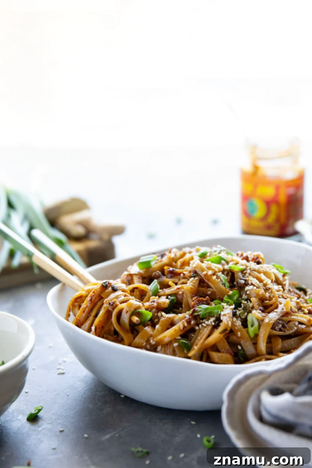 Zingy Ginger Chili Crisp Noodles 2 A vibrant bowl of Ginger Chili Crisp Noodles, showcasing tender rice noodles coated in a rich, spicy sauce with fresh green onions and sesame seeds. This quick and easy 20-minute meal is a perfect takeout alternative.