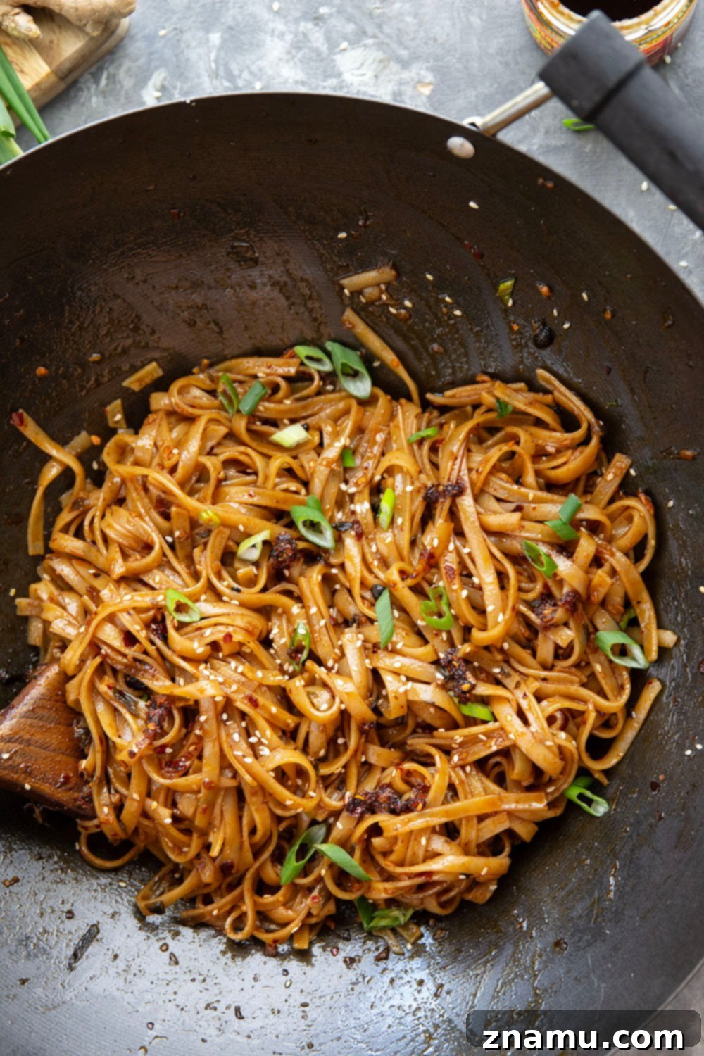 Zingy Ginger Chili Crisp Noodles 4 Ingredients for Ginger Chili Crisp Noodles laid out on a wooden surface, including fresh ginger, garlic, green onions, chili crisp, soy sauce, and rice noodles. Emphasizes fresh, simple ingredients for a quick meal.