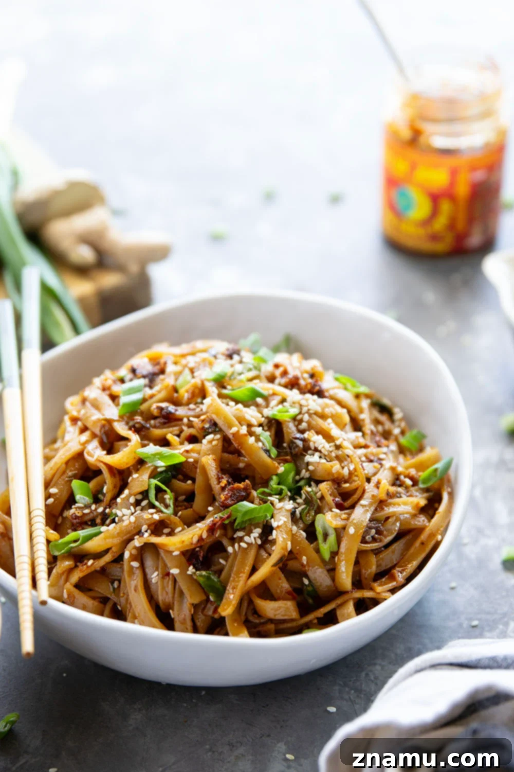 Zingy Ginger Chili Crisp Noodles 5 A serving of Ginger Chili Crisp Noodles in a bowl, garnished with extra chili crisp, green onions, and sesame seeds. The image highlights the delicious texture and spicy appeal of this homemade Asian noodle dish.