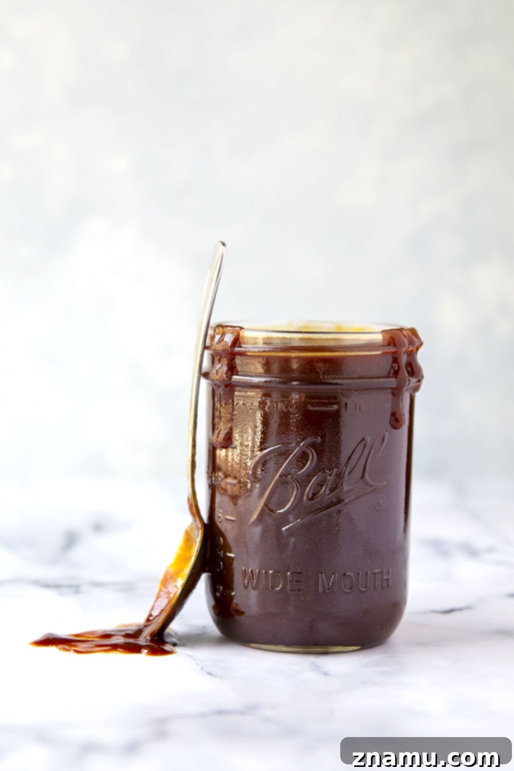 A close-up of a spoon dipping into a jar of thick, dark homemade BBQ sauce, showcasing its rich texture.