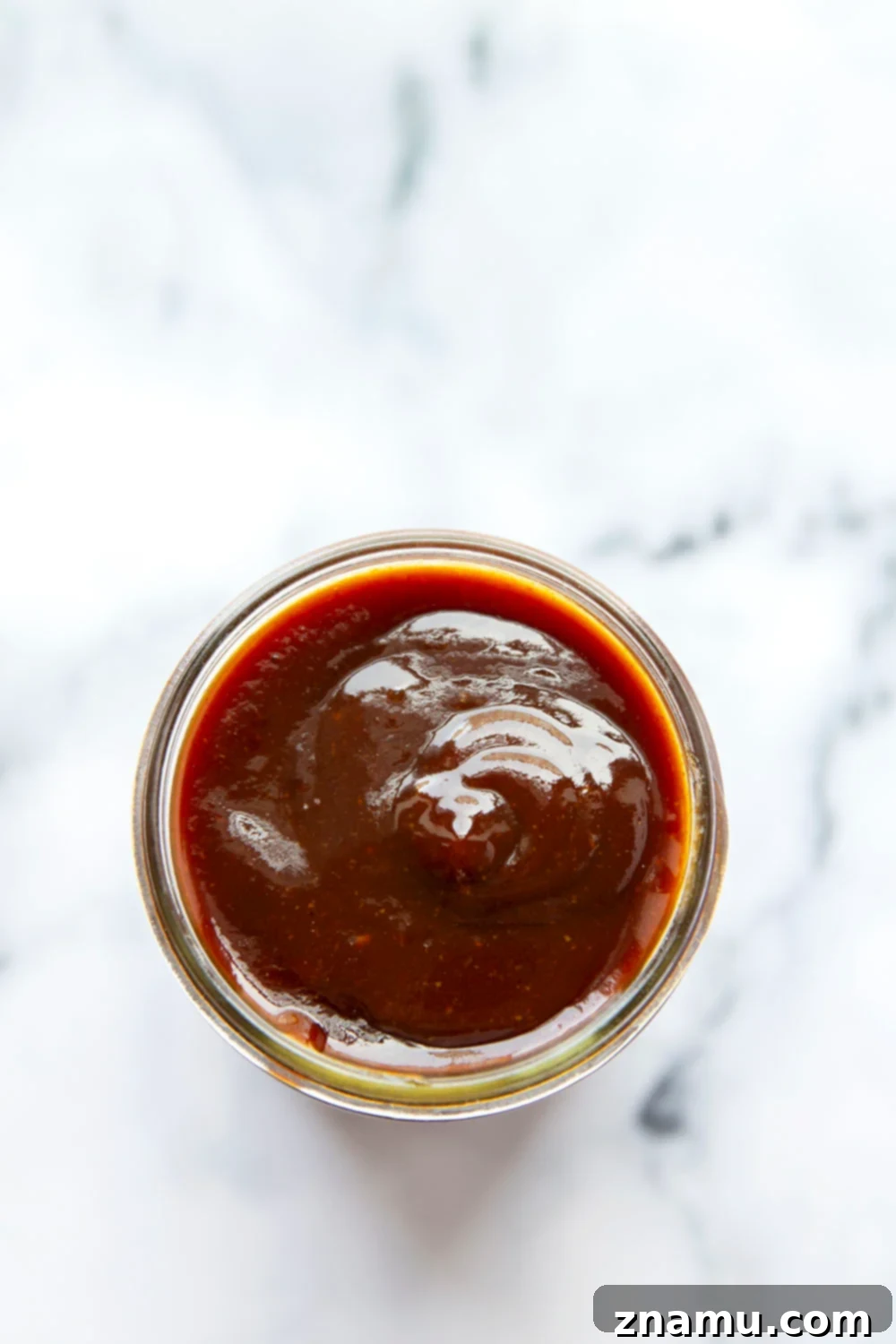 A hand brushing rich homemade BBQ sauce onto grilled chicken, highlighting its perfect consistency and appealing color.