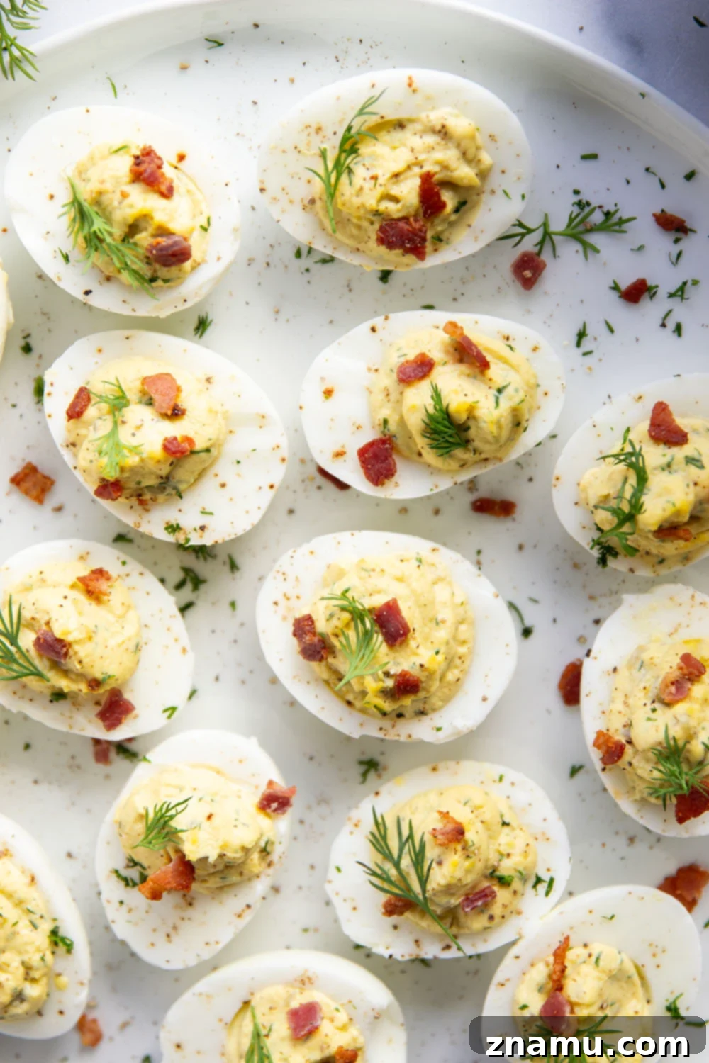 Zesty Bacon Dill Pickle Deviled Eggs 4 A tray of dill pickle deviled eggs ready for serving, garnished with dill and bacon.