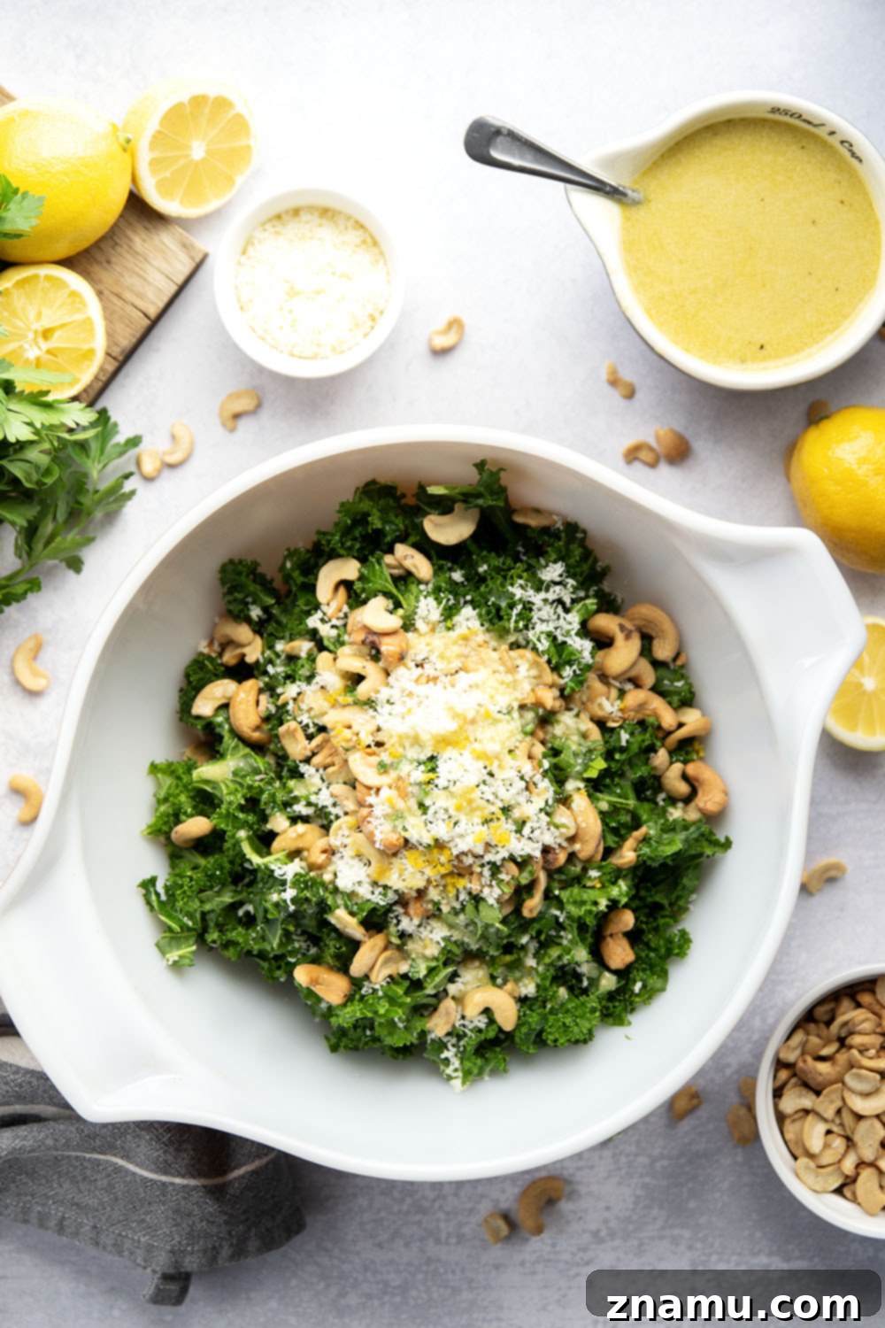 Lemon Kissed Asiago Cashew Kale 3 Close-up of the Asiago Lemon Cashew Kale Salad, showcasing the bright green kale leaves, golden cashews, and white shreds of Asiago cheese.