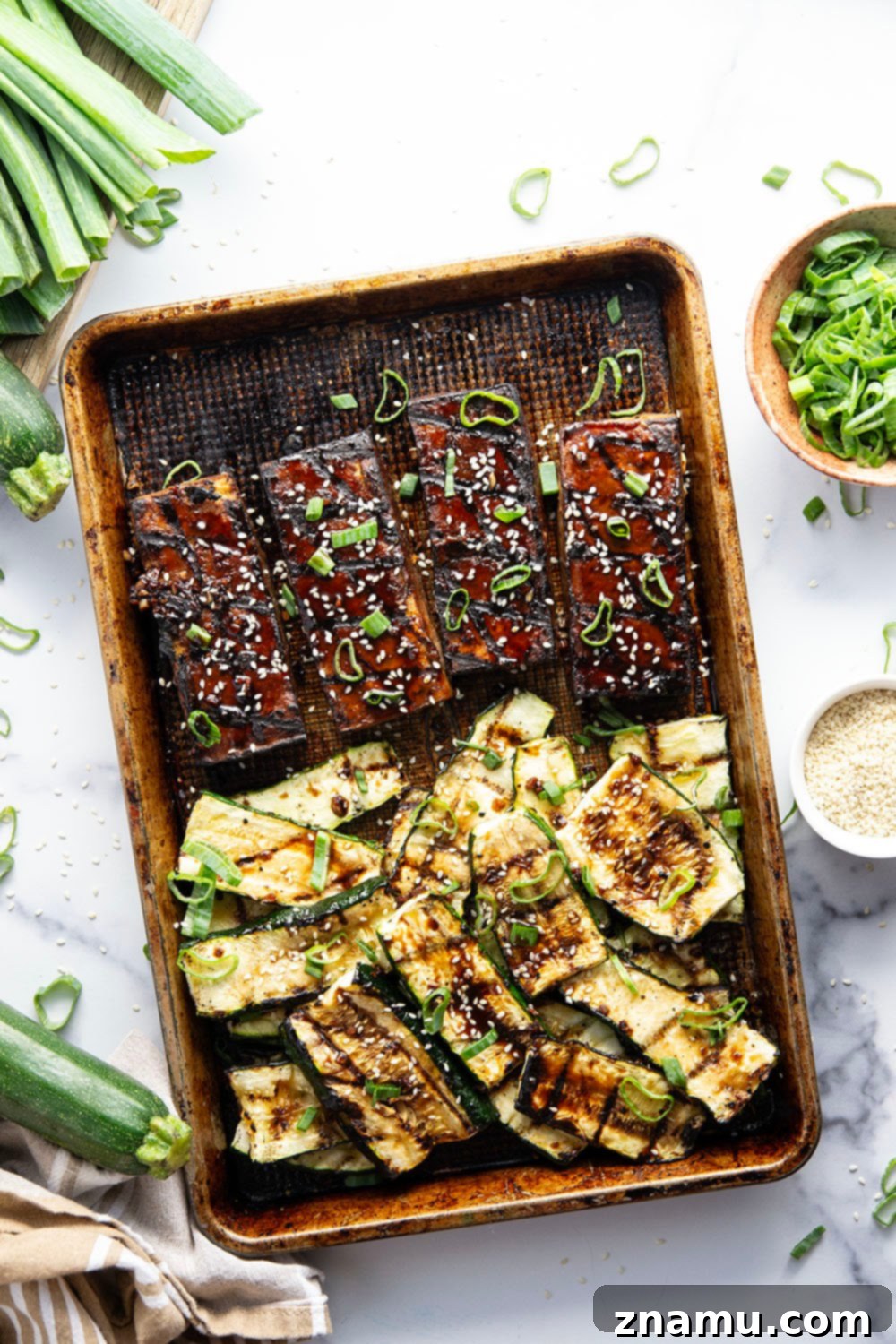 Platter of marinated grilled tofu and zucchini, garnished with green onions and sesame seeds.