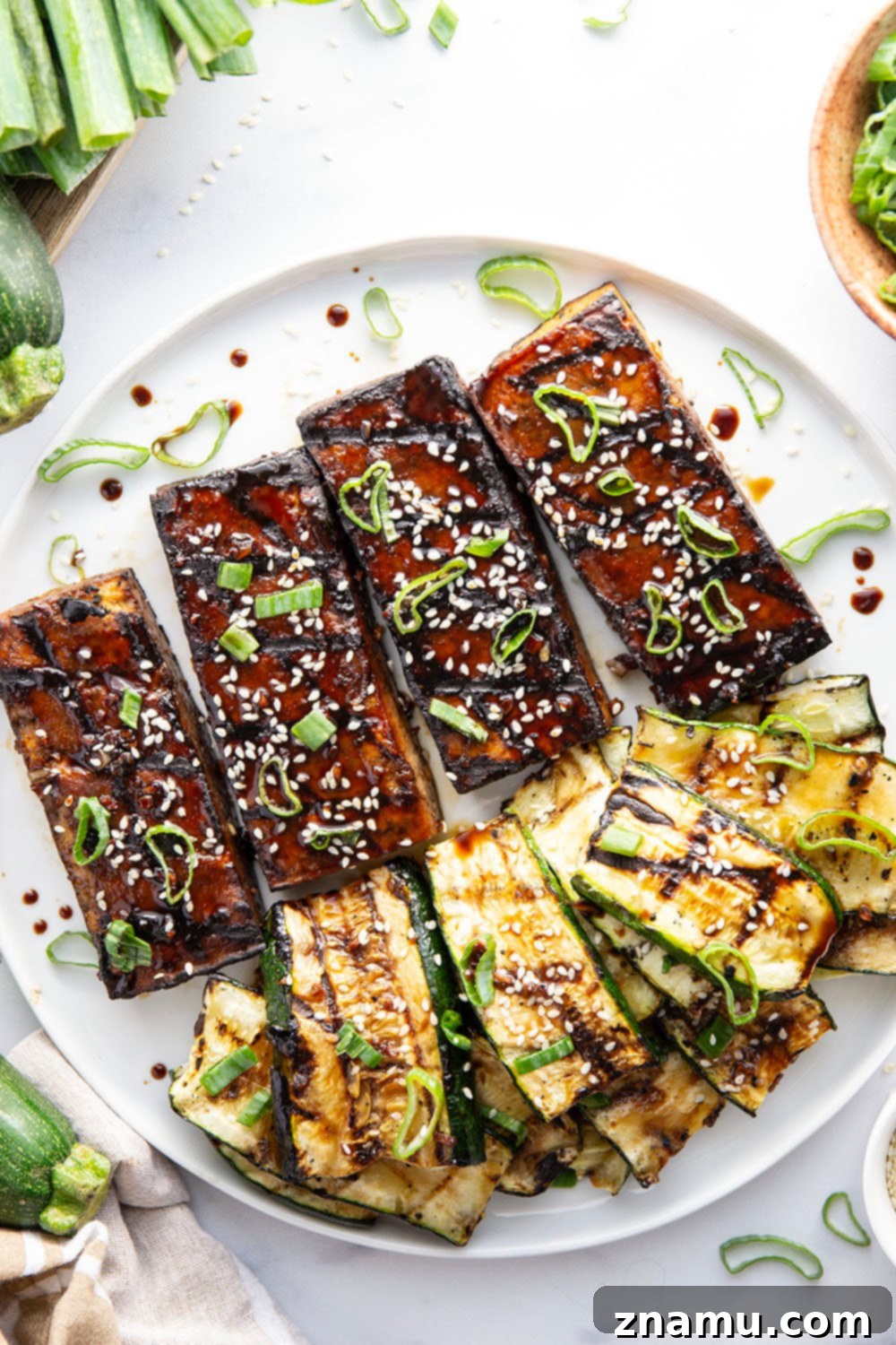 Serving platter with marinated grilled tofu and zucchini, garnished with green onions and sesame seeds.