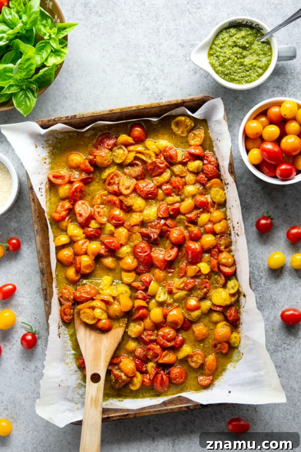 Roasted Cherry Tomato Pesto Pasta 3 Overhead view of a baking sheet filled with halved cherry tomatoes tossed with green pesto, ready for roasting. The tomatoes are plump and colorful.