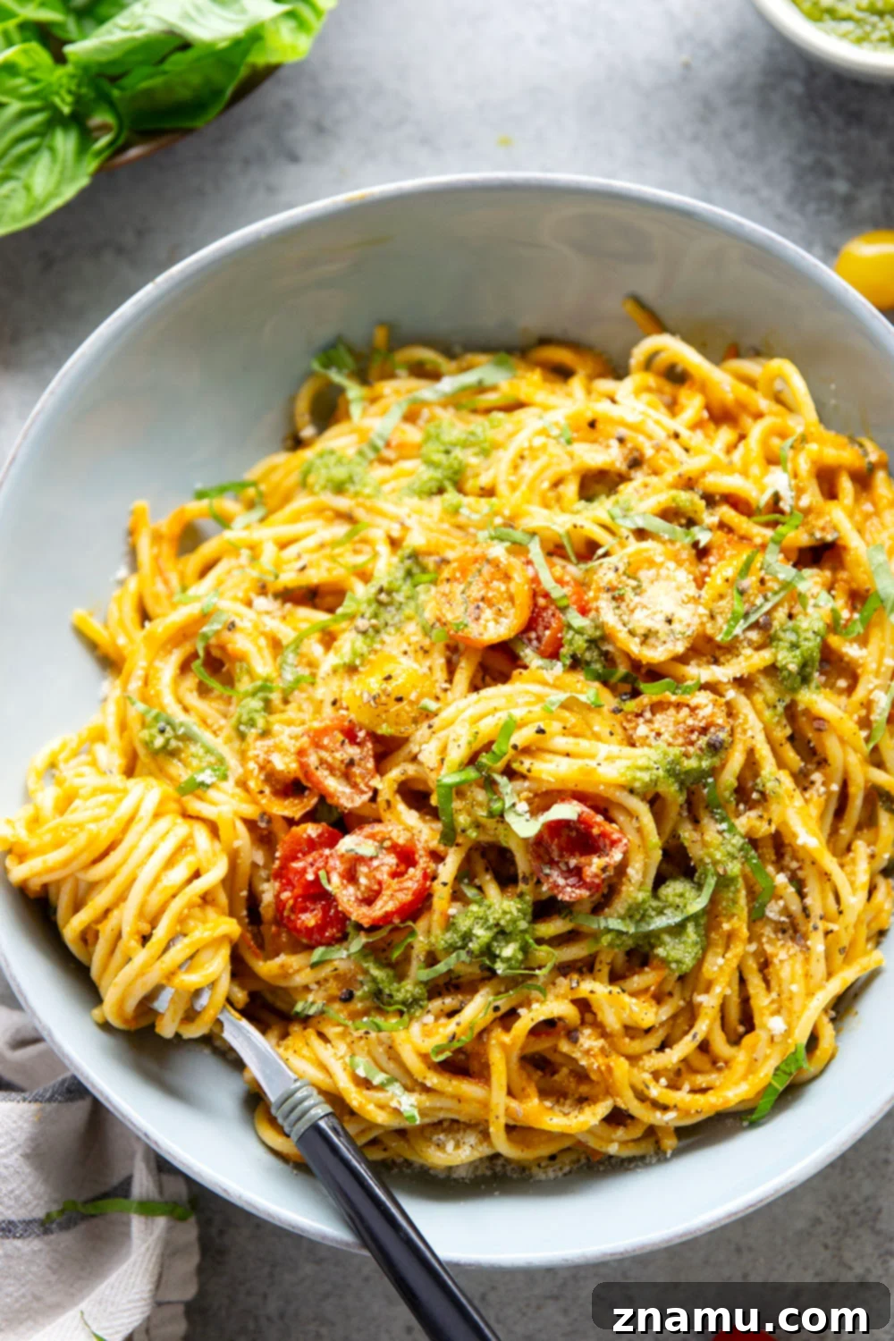 Roasted Cherry Tomato Pesto Pasta 5 Close-up of a wooden spoon scooping roasted cherry tomatoes from a pan into a blender, showcasing the rich, softened texture of the tomatoes.