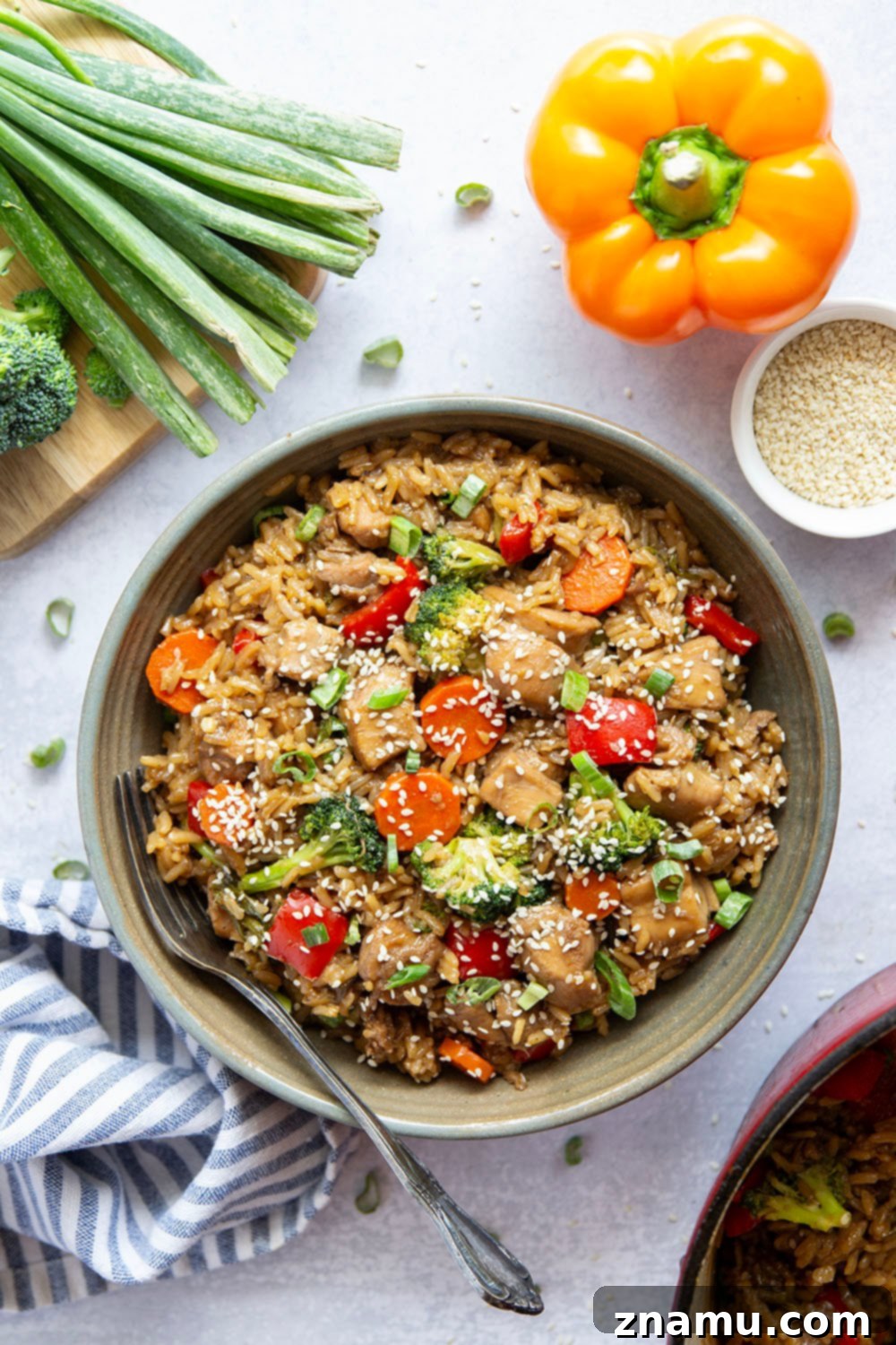 Close-up of succulent teriyaki chicken pieces mixed with fluffy rice and colorful vegetables in a pot.