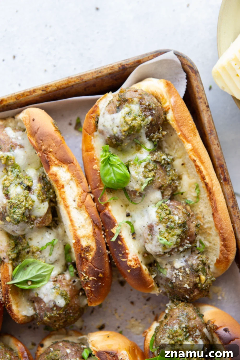 Close-up of a delectable pesto meatball sandwich oozing with melted Havarti cheese and fresh basil.