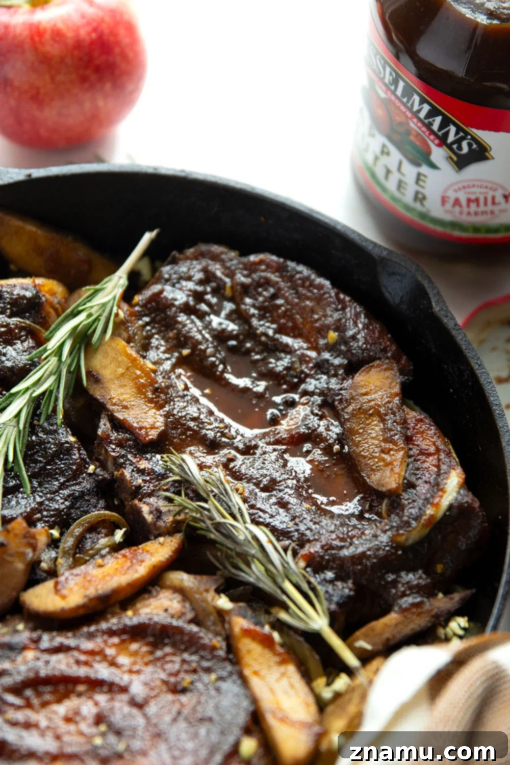 Sticky Apple Butter Pork Chops 3 Overhead view of a cast iron skillet filled with glazed apple butter pork chops, roasted apple slices, and caramelized onions, garnished with fresh rosemary.
