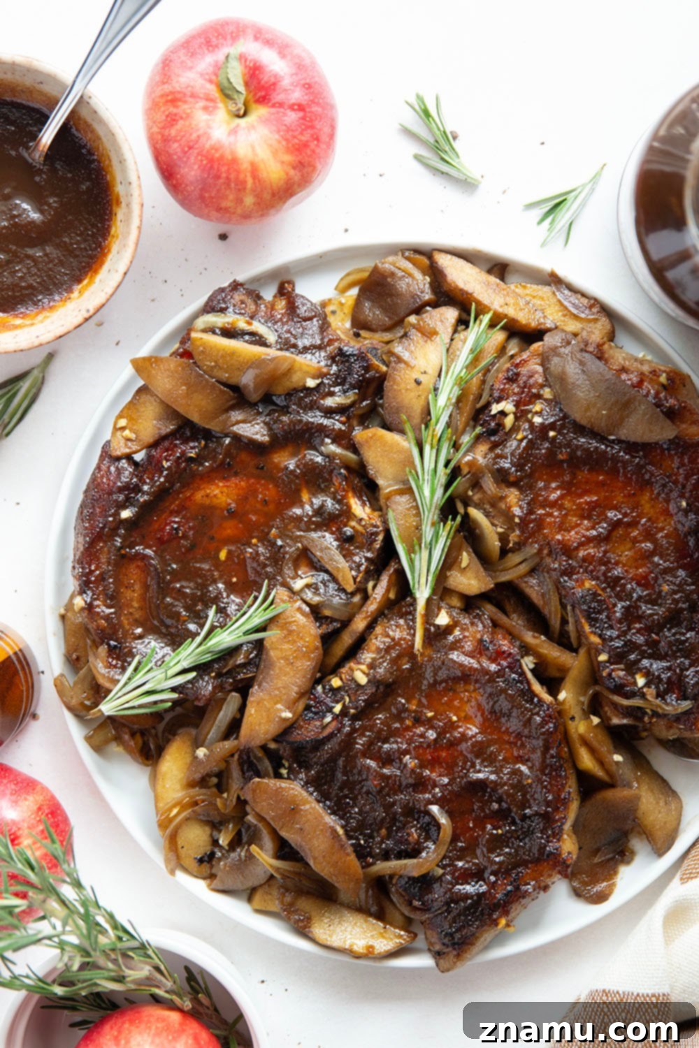 Sticky Apple Butter Pork Chops 4 A close-up of a single apple butter glazed pork chop on a plate, showing its perfectly seared crust and juicy interior, with roasted apples and onions in the background.