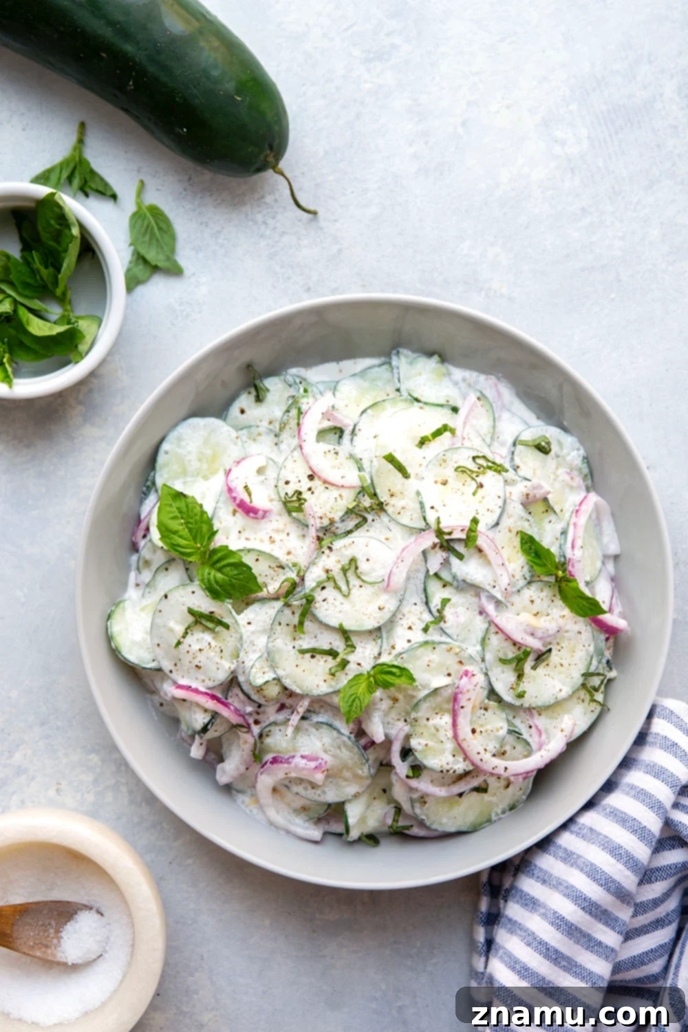 Velvety Basil Cucumber Delight 5 A vibrant bowl of creamy basil cucumber salad, featuring thin slices of cucumber and red onion, generously coated in dressing, with fresh basil leaves sprinkled throughout.