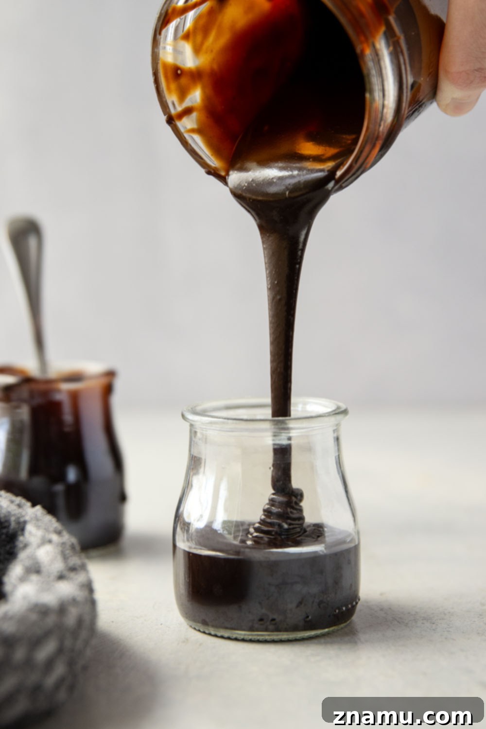 Decadent Homemade Hot Fudge Sauce 6 A thick stream of homemade hot fudge sauce pouring into a glass jar.