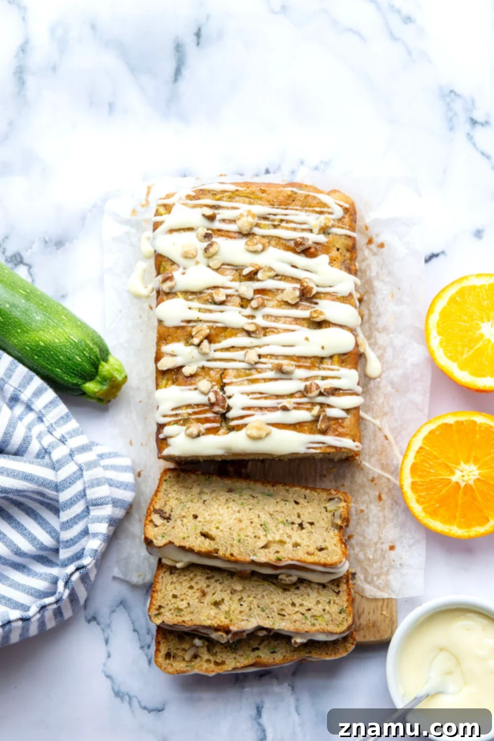 A beautifully baked loaf of moist zucchini bread, generously drizzled with a vibrant orange cream cheese glaze, sitting on a rustic wooden board.