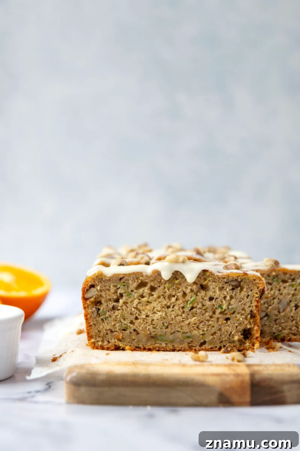 A cross-section of moist zucchini bread showing its tender crumb and pieces of toasted walnuts, ready for glazing.