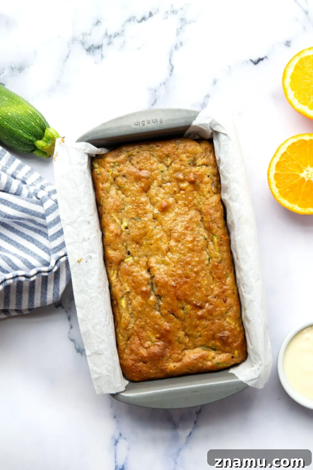 Close-up of the orange cream cheese glaze being drizzled artfully over a loaf of zucchini bread.