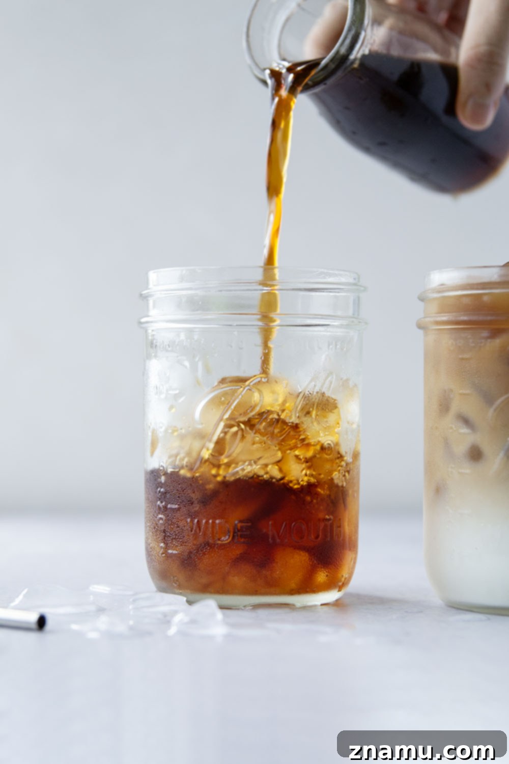 Ultimate Iced Coffee 5 Hands pouring brewed coffee into a glass with ice, preparing an iced coffee.