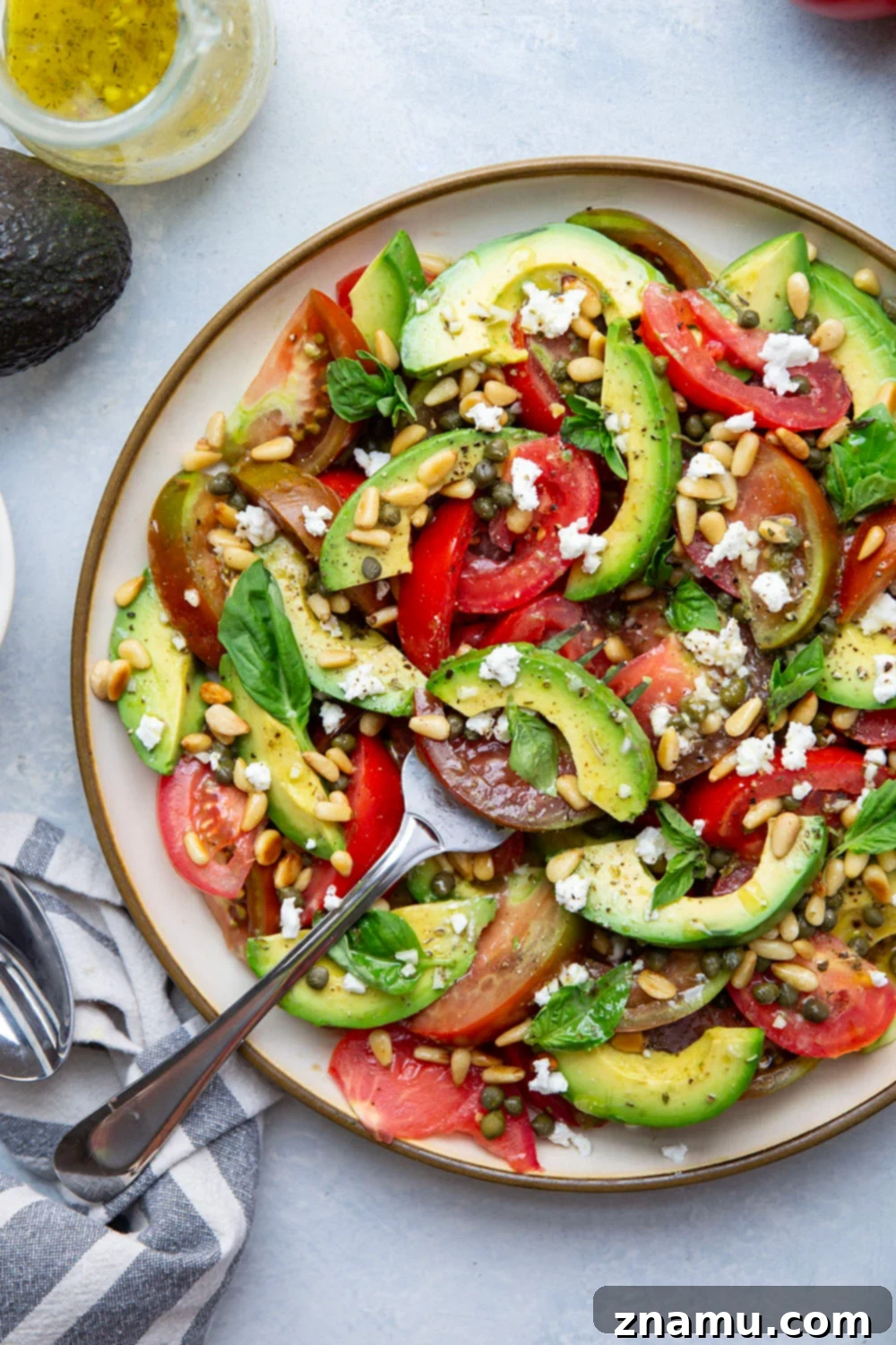 Vibrant Avocado Tomato Salad 4 Fresh basil leaves, feta cheese, and pine nuts topping a vibrant avocado tomato salad.