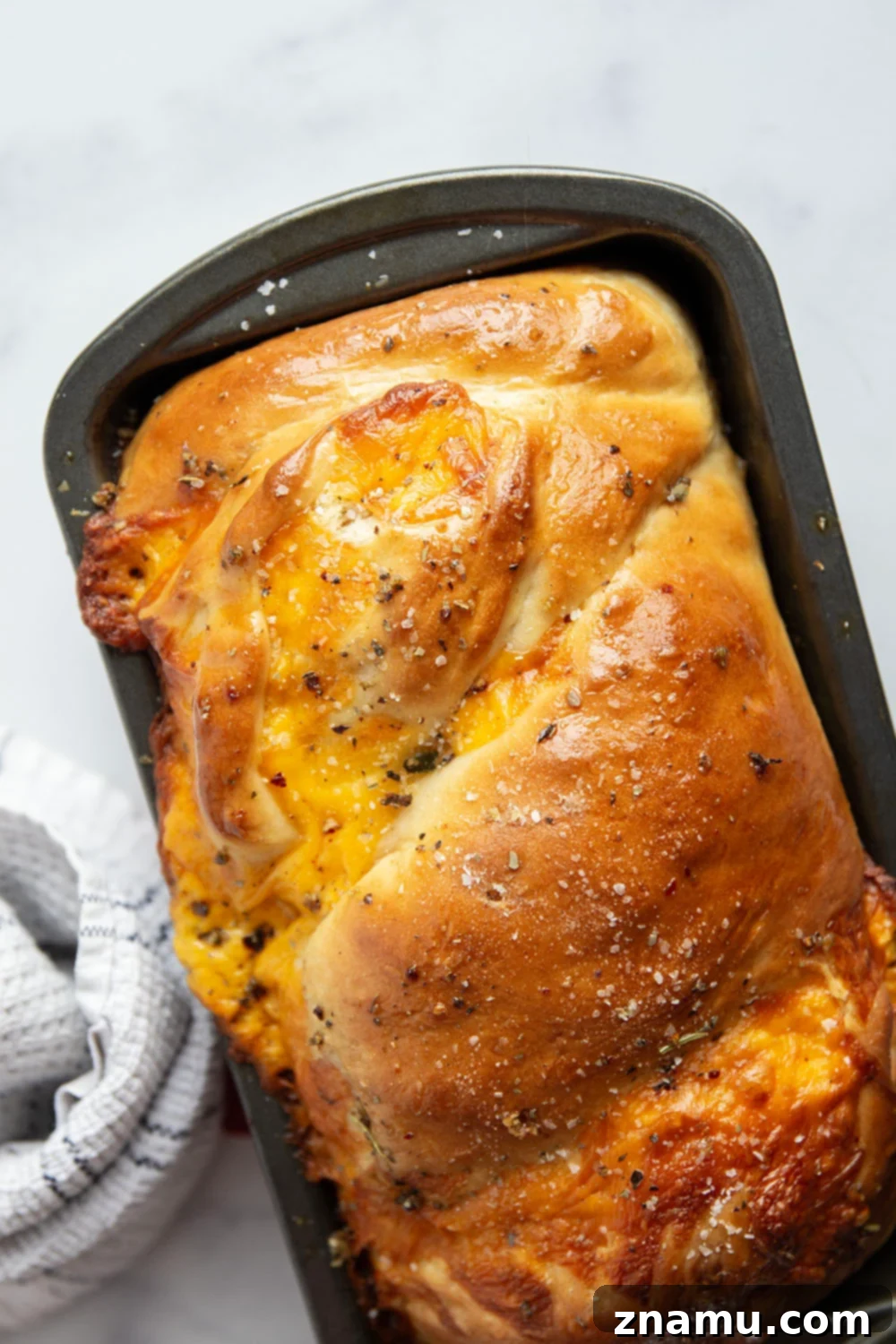Irresistible Homemade Cheese Bread 6 The shaped cheese bread loaf, twisted and ready for its second rise in a loaf pan, showing off the visible cheese within the dough.