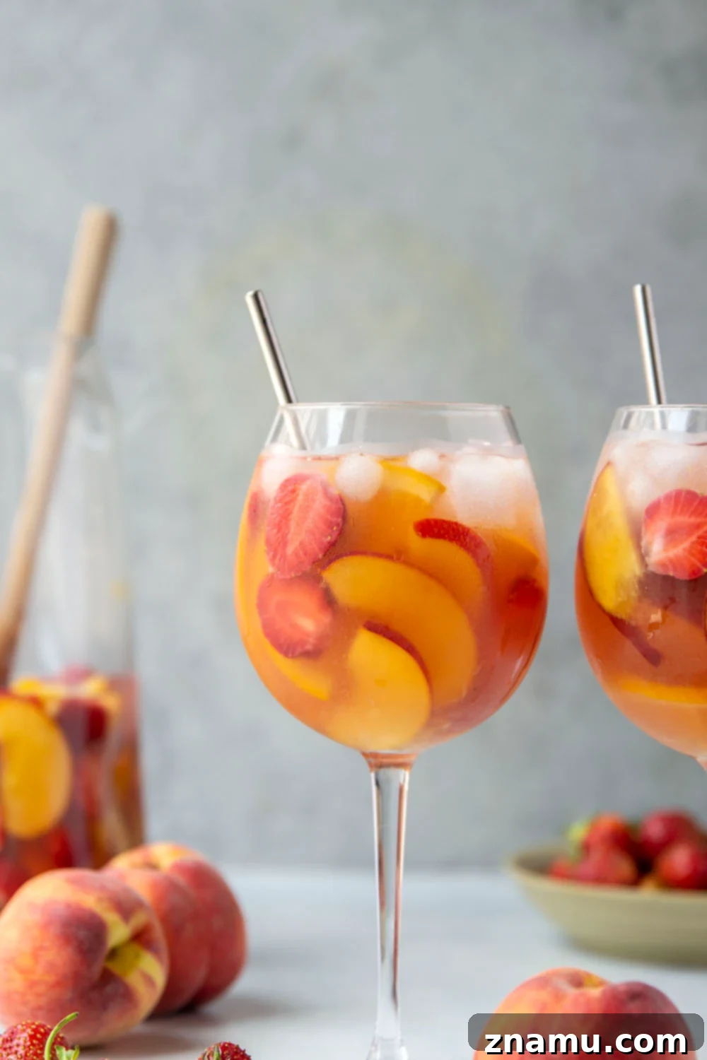Sun-Kissed Peach Strawberry Sangria 4 Hands pouring the vibrant Strawberry Peach Sangria from a large pitcher into a wine glass, filled with ice and fresh fruit, on a sunny outdoor setting.