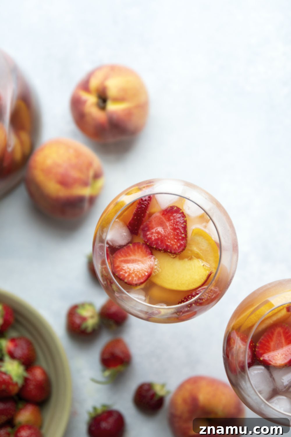 Sun-Kissed Peach Strawberry Sangria 6 A close-up of a glass of Strawberry Peach Sangria, garnished with a mint sprig, sitting on a wooden surface, highlighting the drink's vibrant appeal.