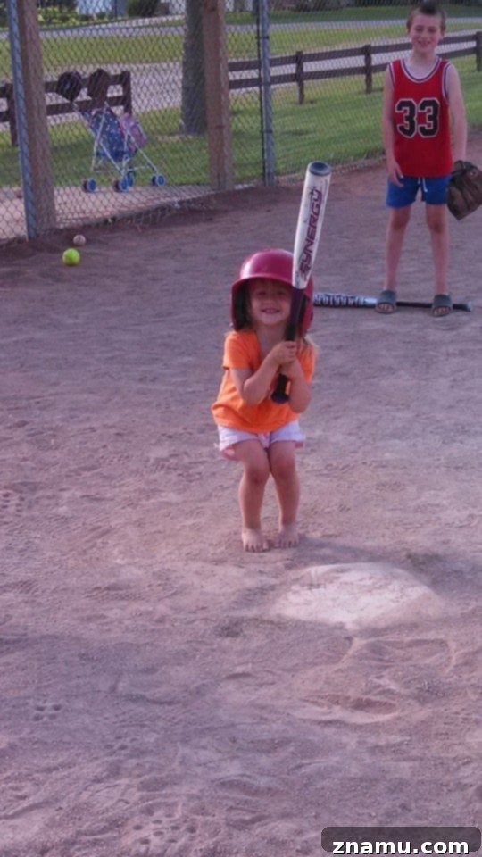Reliving Summer 2014 7 Three-year-old Josie, holding a baseball bat and wearing a cap, stands ready to bat at a family baseball game.