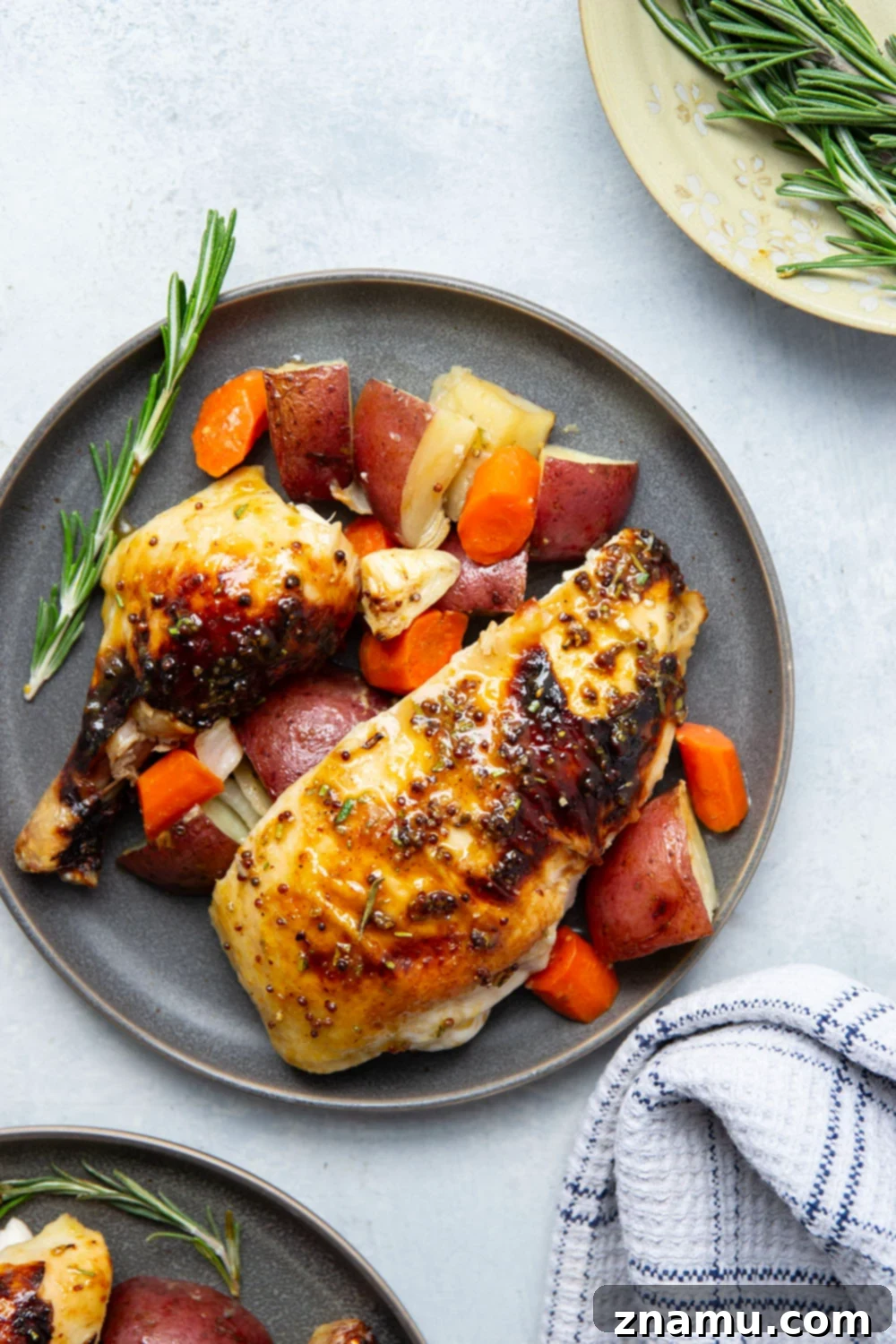 Close-up of crispy, glazed honey mustard roast chicken skin with herbs and perfectly cooked vegetables.