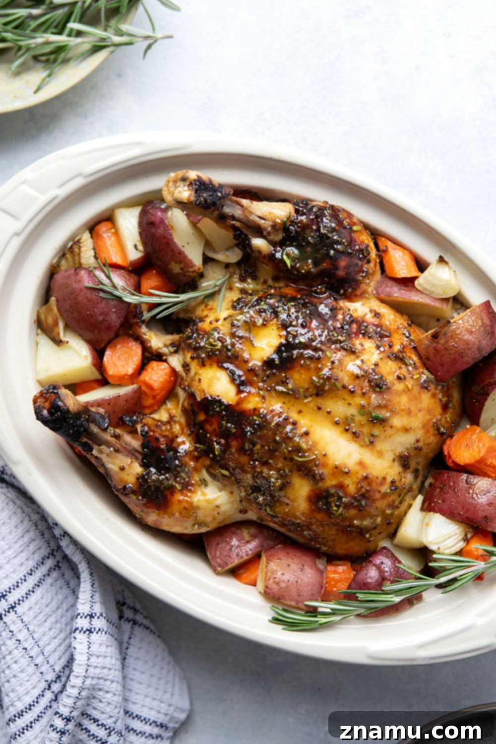 Side view of honey mustard roast chicken on a platter, showcasing the golden-brown skin and a single rosemary sprig.