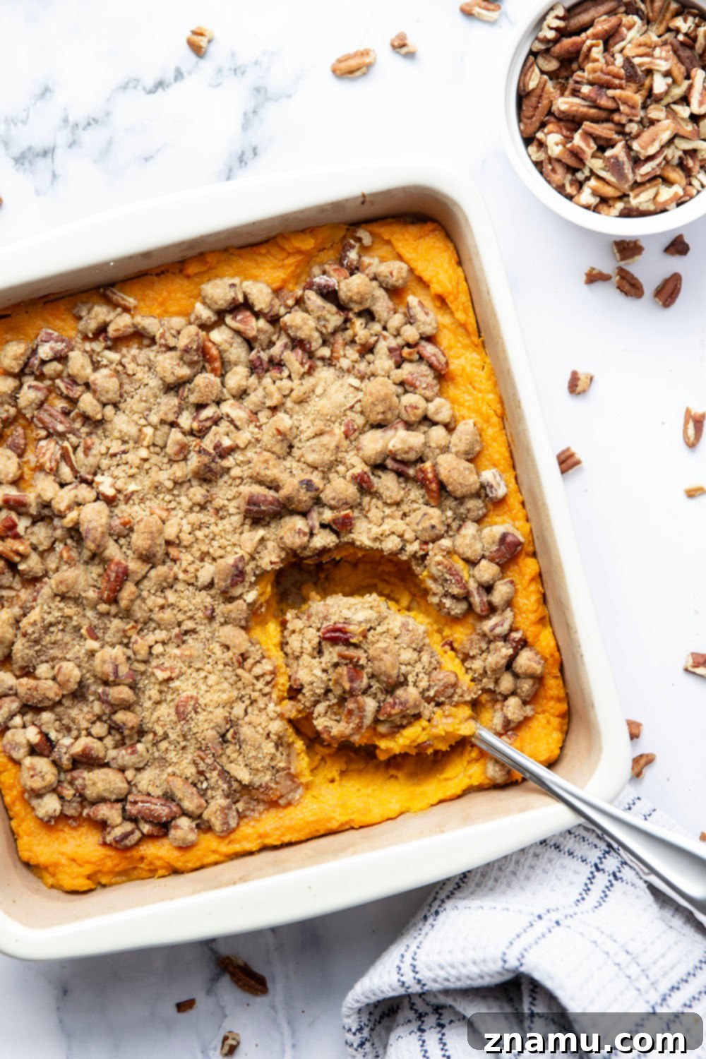 Velvety Sweet Potato Bake with Crunchy Pecan Topping 5 Ingredients for sweet potato casserole laid out on a kitchen counter: sweet potatoes, butter, brown sugar, eggs, vanilla, milk, salt, flour, pecans, and cinnamon.