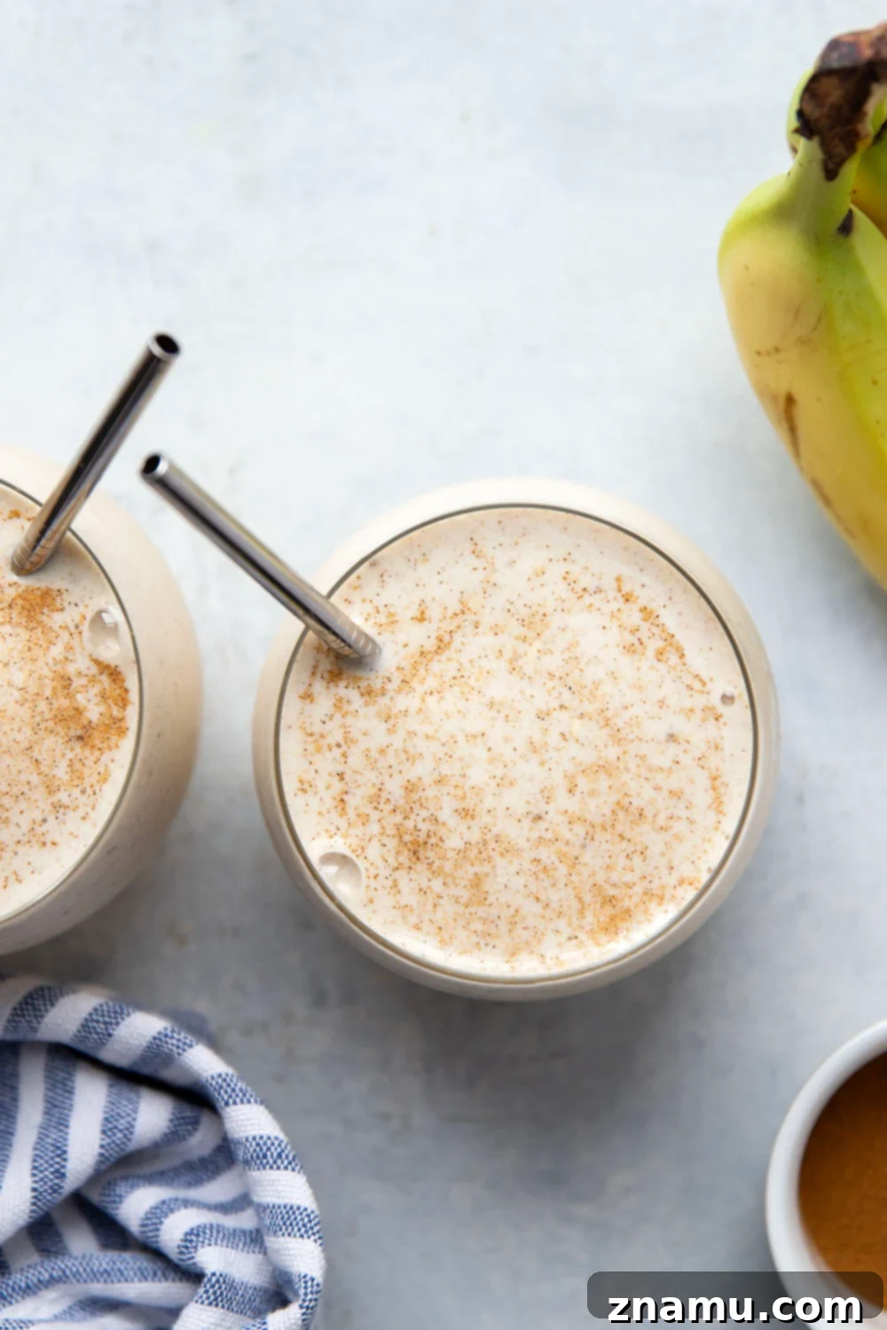 Spiced Banana Bliss Smoothie 2 A tall glass of creamy banana chai smoothie garnished with cinnamon and a whole star anise, sitting on a rustic wooden surface next to some fresh bananas and spices.