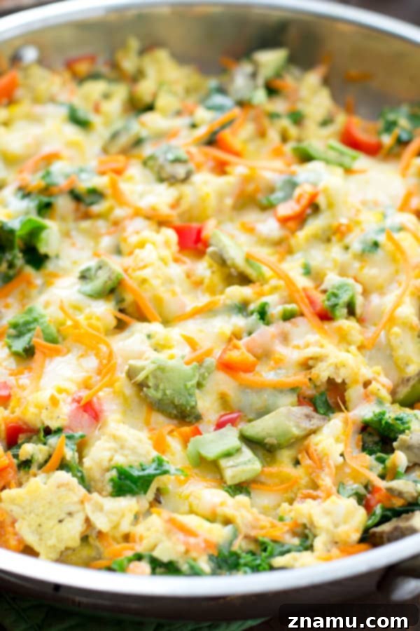 Scrambled eggs with various vegetables and melted cheese in a non-stick pan