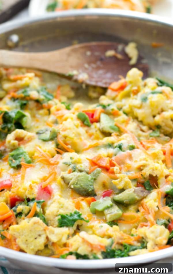 Close-up of Rainbow Veggie Scrambled Eggs topped with melted cheese and fresh avocado