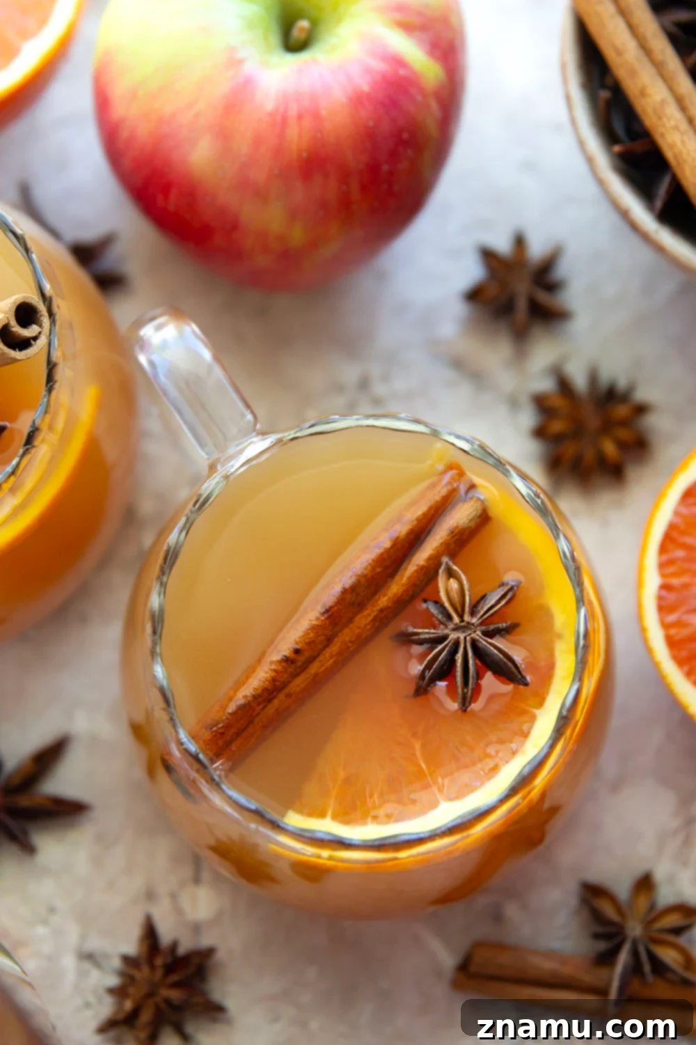Chai-Spiced Apple Cider 4 Pouring Chai Mulled Apple Cider from a pot into a glass, garnished with an orange slice.